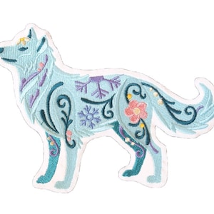 以下が含まれることがあります： 花柄と雪の結晶のデザインが施された、青い刺繍のアイロン接着パッチ。狼が描かれています。