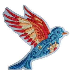 Puede incluir: Parche bordado para planchar con un pájaro azul con alas rojas, naranjas y amarillas. El pájaro está volando con las alas extendidas. El pájaro tiene un diseño detallado con remolinos y flores.