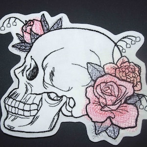 May include: A white embroidered skull with black stitching is adorned with pink and red roses and leaves. The skull is facing to the right and has a detailed design.