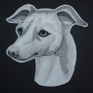 Könnte beinhalten: Gestickter Aufnäher mit einem detaillierten, graustufigen Porträt eines Hundekopfes im Profil. Der Aufnäher hat einen weißen Hintergrund mit aufwendigen Stichen in Grau- und Schwarztönen, die einen strukturierten Effekt erzeugen. Die Merkmale des Hundes sind klar definiert.