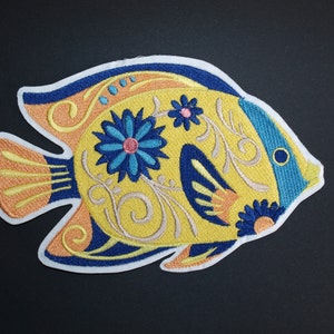 May include: Yellow embroidered fish patch with blue and orange details. The fish has a floral design with a blue flower and swirls.