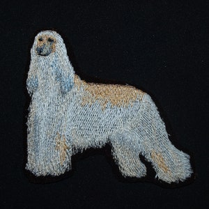 May include: Embroidered patch of a white and tan Afghan Hound with long, flowing hair. The dog is standing with its head held high and its tail curled.