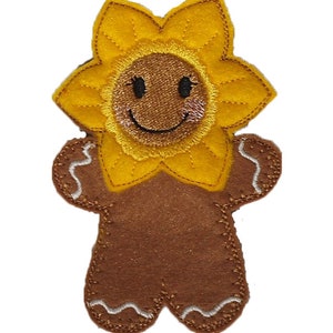 May include: A felt applique of a gingerbread person with a sunflower head. The sunflower has yellow petals and a brown centre with a smiling face. The gingerbread body is brown with white stitching.