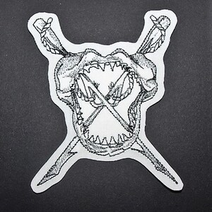 May include: A black and white embroidered patch of a shark's head with crossed swords in its mouth.
