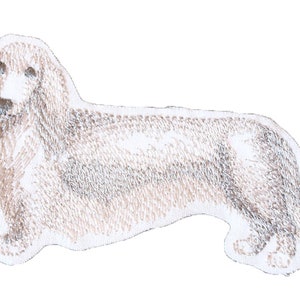 May include: Embroidered patch of a dachshund dog in a light brown color. The dog is facing to the right and is in a standing position.