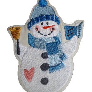 May include: Embroidered iron-on patch of a snowman wearing a blue hat and scarf, holding a bell in one hand and a music note in the other. The snowman has a heart on its belly and three black buttons.