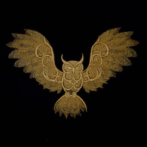 Könnte beinhalten: Eine goldene gestickte Eule mit filigranen Details und ausgebreiteten Flügeln vor schwarzem Hintergrund.