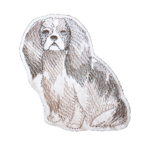May include: Embroidered patch of a brown and white dog with long, flowing hair. The dog is sitting with its head tilted down and its eyes closed.
