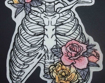 May include: Embroidered patch featuring a detailed anatomical illustration of a ribcage with a floral arrangement of roses and leaves in shades of pink, yellow, and green.