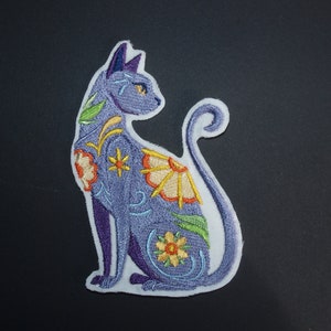 Op de afbeelding: Paarse geborduurde strijkpatch van een kat met bloemmotieven in geel, oranje en groen.