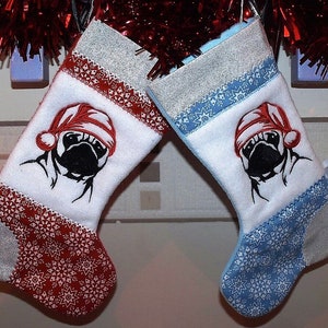 May include: Two Christmas stockings with a white background and a pug dog wearing a Santa hat embroidered on each. One stocking is red with white snowflakes and the other is blue with white snowflakes.