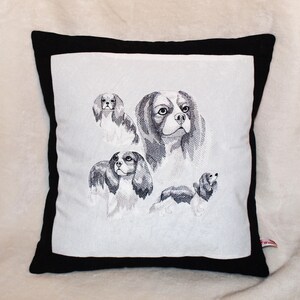 Può includere: Un cuscino bianco con un bordo nero presenta un disegno ricamato di quattro Cavalier King Charles Spaniel in bianco e nero.
