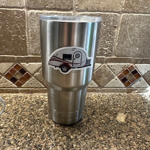 May include: A stainless steel travel mug with a sticker of a white and red camper on it.