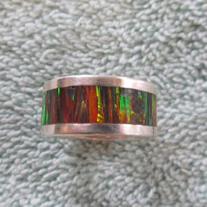 Könnte beinhalten: Ein Silberring mit einem bunten Einlegearbeiten aus Grün, Rot und Orange. Die Einlegearbeiten sind in einem Silberband gefasst.