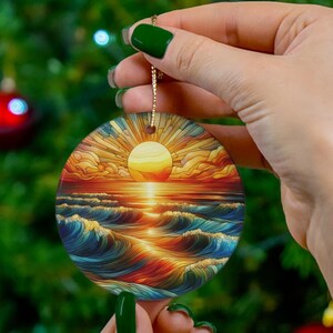 May include: A round ceramic ornament with a colorful sunset over the ocean scene. The ornament features a bright orange sun, blue waves, and a red and orange sky.