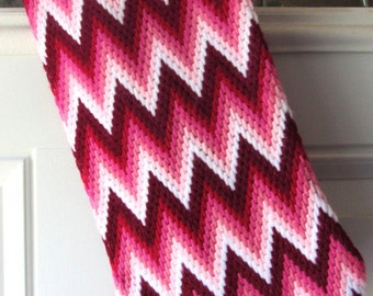 Può includere: Un calzino di Natale a chevron rosa e rosso. Il calzino è in tessuto e presenta un motivo a zig-zag bianco.