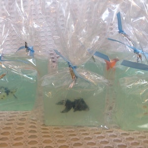 May include: Four clear plastic-wrapped bars of soap with blue ribbon ties. Each bar contains a different coloured fish figurine.