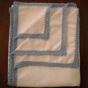 Puede incluir: Una manta blanca doblada con un borde de ganchillo azul claro. La manta est&aacute; hecha de un material suave y tiene un dise&ntilde;o simple y elegante. El borde de ganchillo a&ntilde;ade un toque de encanto hecho a mano.