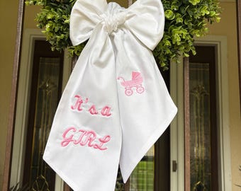 Banda para anunciar el nacimiento de una niña. Esta banda es blanca con un cochecito de bebé rosa y la frase "Es una niña" en los extremos opuestos.