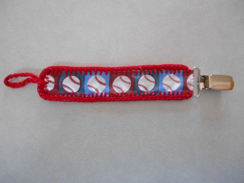 Pacifier clip made of cute baseball print on red and blue ribbon and matching red hand crochet trim.