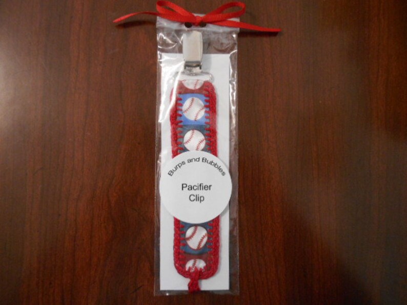 Pacifier clip made of cute baseball print on red and blue ribbon and matching red hand crochet trim.