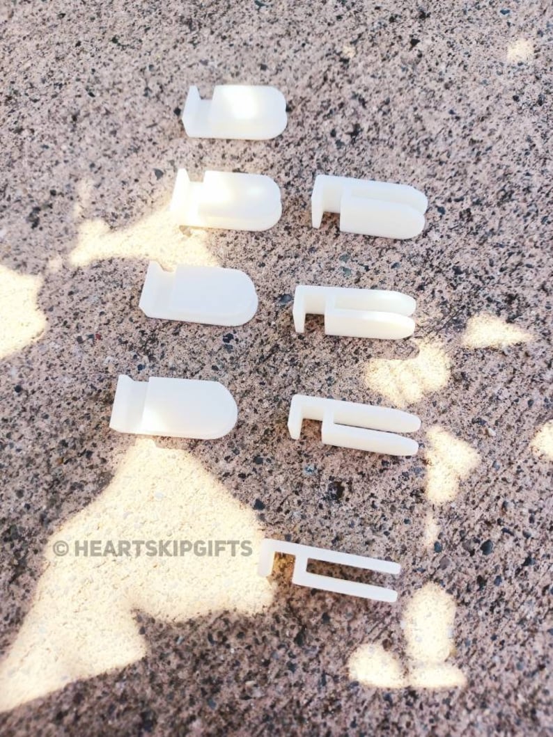 May include: A collection of white plastic curtain clips and hooks, arranged on a textured gray surface. The clips have various designs, including rounded and rectangular shapes. The image includes the text "&copy; HEARTSKIPGIFTS".