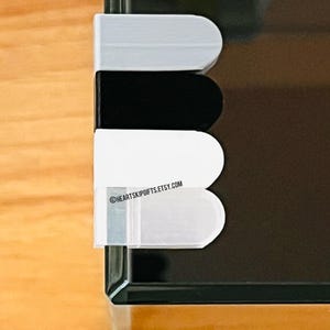 May include: A close-up of a black, white, and gray object with rounded edges. The object is attached to a black surface. The text "HEARTSKIPGIFTS.ETSY.COM" is visible on the object.