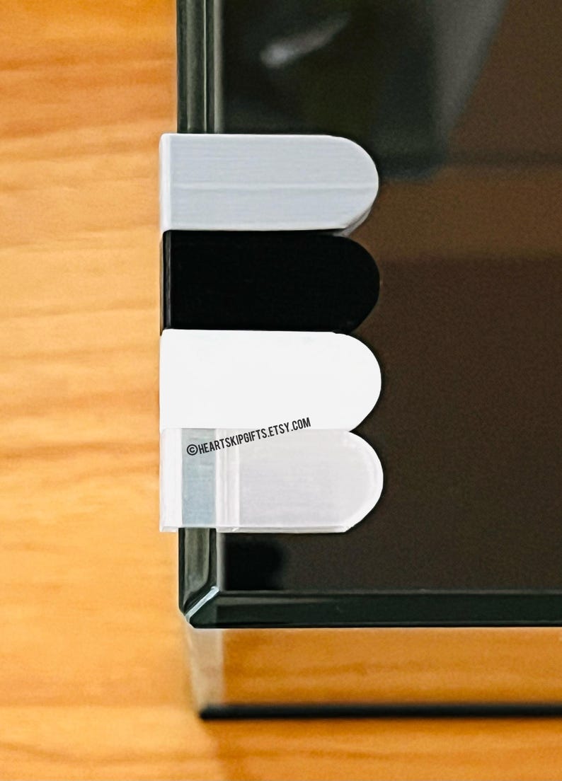 May include: A close-up of a black, white, and gray object with rounded edges. The object is attached to a black surface. The text "HEARTSKIPGIFTS.ETSY.COM" is visible on the object.