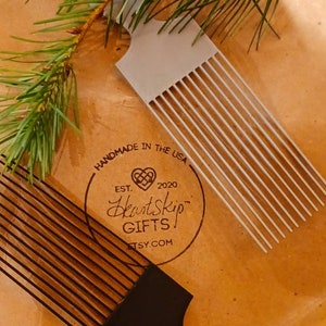 May include: Two combs, one black and one gray, with a brown paper background. The paper has a logo that says "HeartSkip Gifts" with a heart and the text "Handmade in the USA, Est. 2020, Etsy.com".