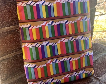 Puede incluir: Una funda de libro colorida con un patrón repetido de libros apilados en estanterías. Los libros tienen lomos de varios colores, incluyendo rojo, amarillo, verde, azul y morado. El fondo es de color marrón claro.