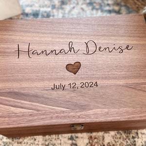 May include: A wooden keepsake box with a personalized inscription that reads "Hannah Denise" and "July 12, 2024". The box has a heart-shaped cutout and a brass latch.