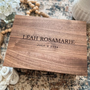 May include: A wooden keepsake box with the inscription "LEAH ROSAMARIE JULY 9 2024" engraved on the top.