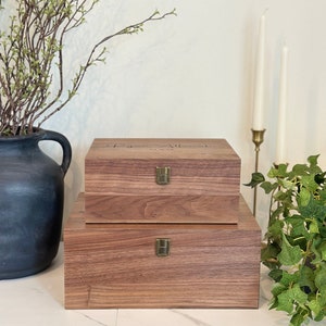 May include: Two wooden boxes with brass hinges and latches. The top box has the text "The Allens" engraved on the lid. The boxes are sitting on a white marble surface.