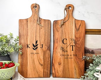 May include: Two wooden cutting boards with engraved initials and a leafy design. The first board has the initials "K J" and the text "EST. 2025". The second board has the initials "C T" and the text "COLLIN & TEE EST. 2025".