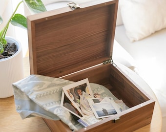 May include: A wooden box with a hinged lid, open to reveal a collection of photographs and a blue patterned fabric inside.