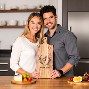 A happy couple holding a personalized cutting board with their initials and wedding date in a modern kitchen setting.