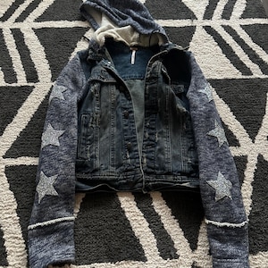 May include: A blue denim jacket with a hooded sweatshirt attached to the sleeves. The sleeves have silver glitter stars on them.