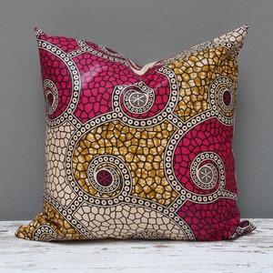 May include: A decorative pillow with a geometric pattern in shades of pink, gold, and cream. The pattern features circles and swirls.
