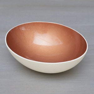 May include: A white ceramic bowl with a copper-colored interior. The bowl is oval shaped and has a smooth, glossy finish.