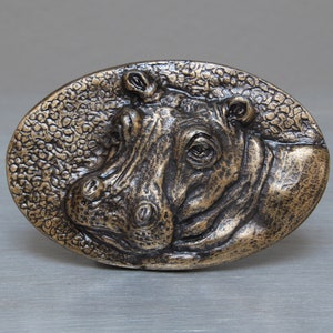 May include: A bronze-coloured metal belt buckle featuring a detailed, three-dimensional hippopotamus head design.