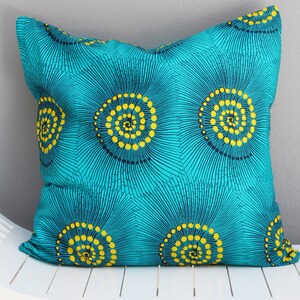 Può includere: Un cuscino blu turchese con un motivo geometrico di cerchi gialli e blu scuro. I cerchi sono disposti a spirale.