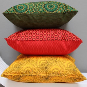 Può includere: Tre cuscini decorativi impilati uno sopra l'altro. Il cuscino superiore è verde con un motivo dorato, il cuscino intermedio è rosso con un motivo bianco e il cuscino inferiore è giallo con un motivo nero.