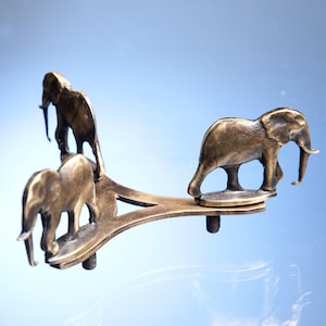 May include: A brass decorative stand with three elephant figurines. The stand has a Y-shaped base and each elephant is positioned on a separate arm.