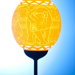 May include: A yellow carved gourd lamp with a rhinoceros design. The lamp is on a black stand.