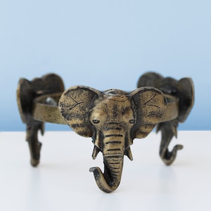 May include: A gold metal decorative stand with three elephant head legs. The stand has a round top and is perfect for displaying a plant or other decorative items.
