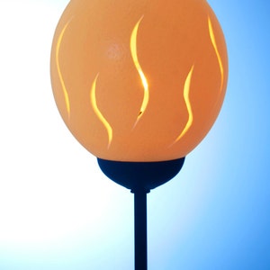 Può includere: Una lampada realizzata con un uovo di struzzo intagliato con un supporto in metallo nero. L'uovo è illuminato dall'interno, creando un bagliore caldo.