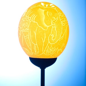 May include: A yellow lampshade with an elephant carved into it. The lampshade is on a black stand.