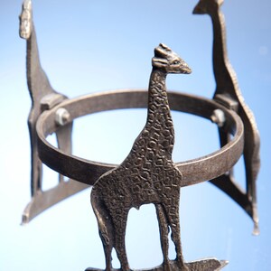May include: A metal stand with three giraffe figures forming the base. The stand is circular and has a textured surface.