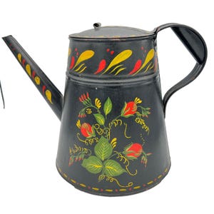 May include: A black metal teapot featuring a hand-painted floral design with red rosebuds and green leaves on the body. The spout and lid are decorated with yellow and red brushstroke patterns. It includes a curved handle and a fitted lid.