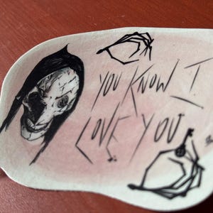 May include: A sticker with a black and white illustration of a person with a skull-like face and the text "You Know I Love You".
